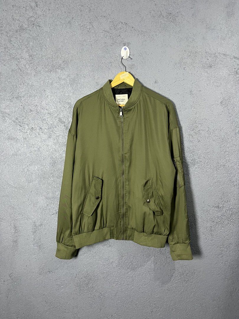 Natural Story Olive Green Bomber Jacket (Category: Coats, Jackets and Outerwear) located in Famy. Submitted by basicthrifted (Listing ID 1469236142, Image 1). Description: - Brand: Natural Story - Color: Olive green with black inner lining - Material: 100% Polyester - Closure: Full front zip - Details: Ribbed collar, cuffs, and hem - Pockets: Utility zipper pocket on the left sleeve and two slanted front pockets - Condition: Excellent.
