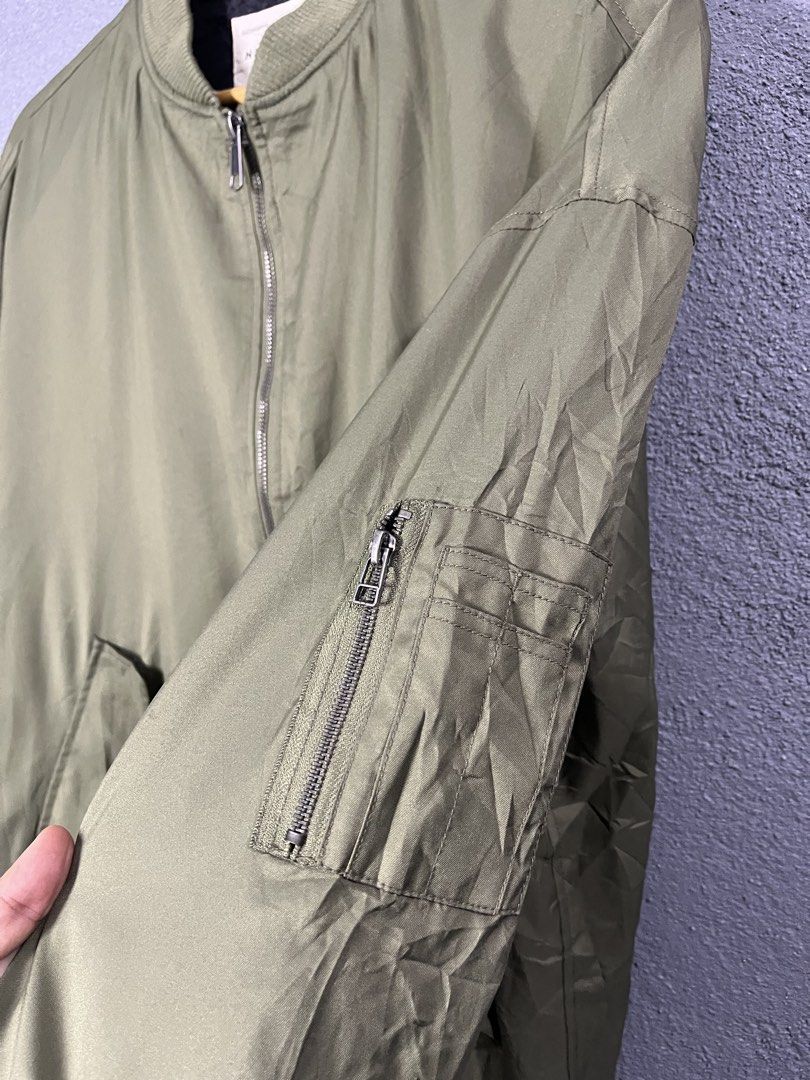 Natural Story Olive Green Bomber Jacket (Category: Coats, Jackets and Outerwear) located in Famy. Submitted by basicthrifted (Listing ID 1469236142, Image 3). Description: - Brand: Natural Story - Color: Olive green with black inner lining - Material: 100% Polyester - Closure: Full front zip - Details: Ribbed collar, cuffs, and hem - Pockets: Utility zipper pocket on the left sleeve and two slanted front pockets - Condition: Excellent.