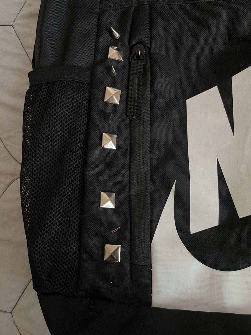Nike Black Backpack with Grunge Emo Skater Silver Studs (Category: Backpacks) located in Quezon City. Submitted by toasterpiee (Listing ID 1469244360, Image 2). Description: - Brand: Nike - Color: Black with a large white front logo - Edgy Details: Metal pyramid studs along the left zipper - Storage: Main zippered compartment & side mesh water bottle pocket - Comfort: Padded standard shoulder straps & sturdy top handle - Flaws: Minor dirt marks o