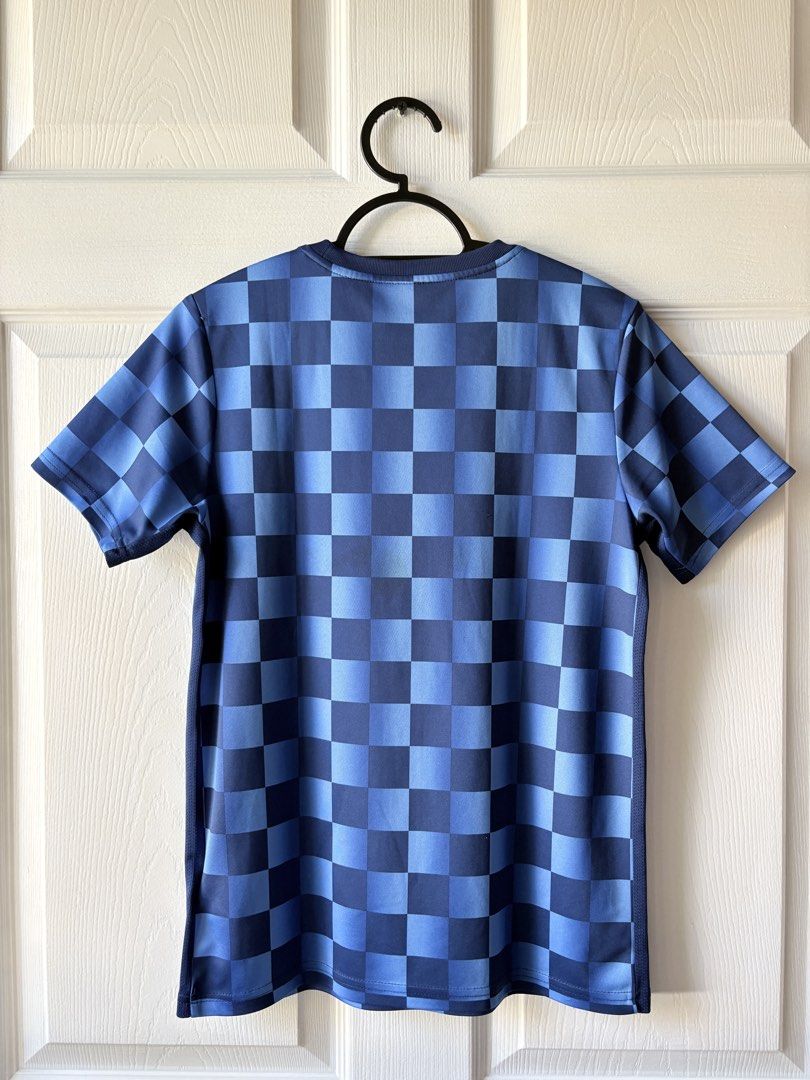 Nike Blue Checkered Football Jersey (Category: Babies & Kids Fashion) located in Liloan. Submitted by mrs.jboiser (Listing ID 1469202940, Image 2). Description: - Brand: Nike - Color: Blue and dark blue checkered pattern - Logo: Orange embroidered Nike swoosh on right chest - Fit: Standard fit jersey with short sleeves and crew neck - Material: Breathable athletic fabric with mesh side panels.