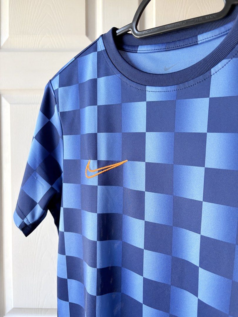 Nike Blue Checkered Football Jersey (Category: Babies & Kids Fashion) located in Liloan. Submitted by mrs.jboiser (Listing ID 1469202940, Image 3). Description: - Brand: Nike - Color: Blue and dark blue checkered pattern - Logo: Orange embroidered Nike swoosh on right chest - Fit: Standard fit jersey with short sleeves and crew neck - Material: Breathable athletic fabric with mesh side panels.