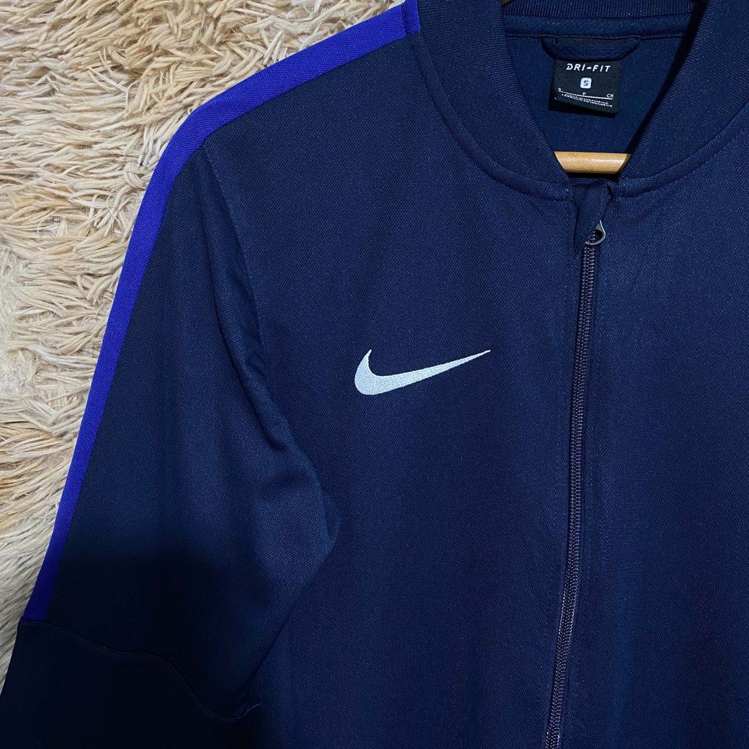 Nike Dri-Fit Navy Blue Track Jacket Size S (Category: Coats, Jackets and Outerwear) located in Butuan. Submitted by jc13thrifts (Listing ID 1469306564, Image 2). Description: - Brand: Nike - Style: Dri-Fit track jacket - Color: Navy blue with contrasting purple sleeve stripes - Logo: White printed swoosh on the chest - Features: Full zip closure, ribbed cuffs and hem, adjustable waist drawstring - Size: Small (S).
