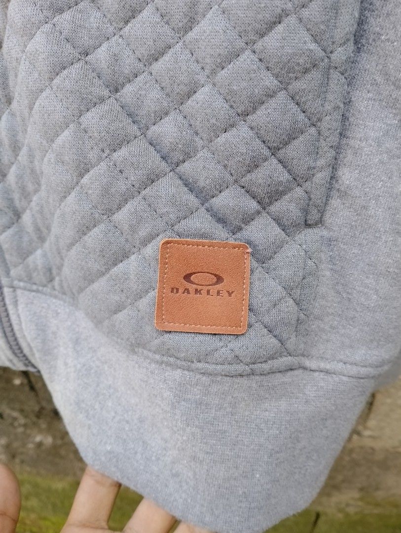 Oakley Quilted Full Zip Hoodie Grey Medium (Category: Coats, Jackets and Outerwear) located in San Ildefonso. Submitted by lanz_baesa (Listing ID 1469318052, Image 3). Description: - Brand: Oakley - Type: Zip hoodie with attached hood - Size: Medium (Regular fit) - Color: Grey - Material: Comfortable cotton and polyester blend - Design details: Quilted pattern on the front and a subtle leather logo patch near the hem - Condition: Good, ideal for 