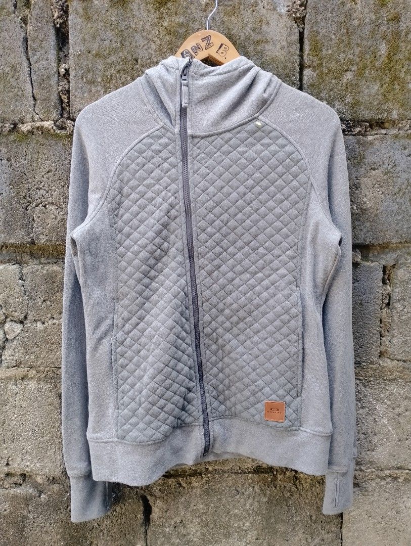 Oakley Quilted Full Zip Hoodie Grey Medium (Category: Coats, Jackets and Outerwear) located in San Ildefonso. Submitted by lanz_baesa (Listing ID 1469318052, Image 1). Description: - Brand: Oakley - Type: Zip hoodie with attached hood - Size: Medium (Regular fit) - Color: Grey - Material: Comfortable cotton and polyester blend - Design details: Quilted pattern on the front and a subtle leather logo patch near the hem - Condition: Good, ideal for 