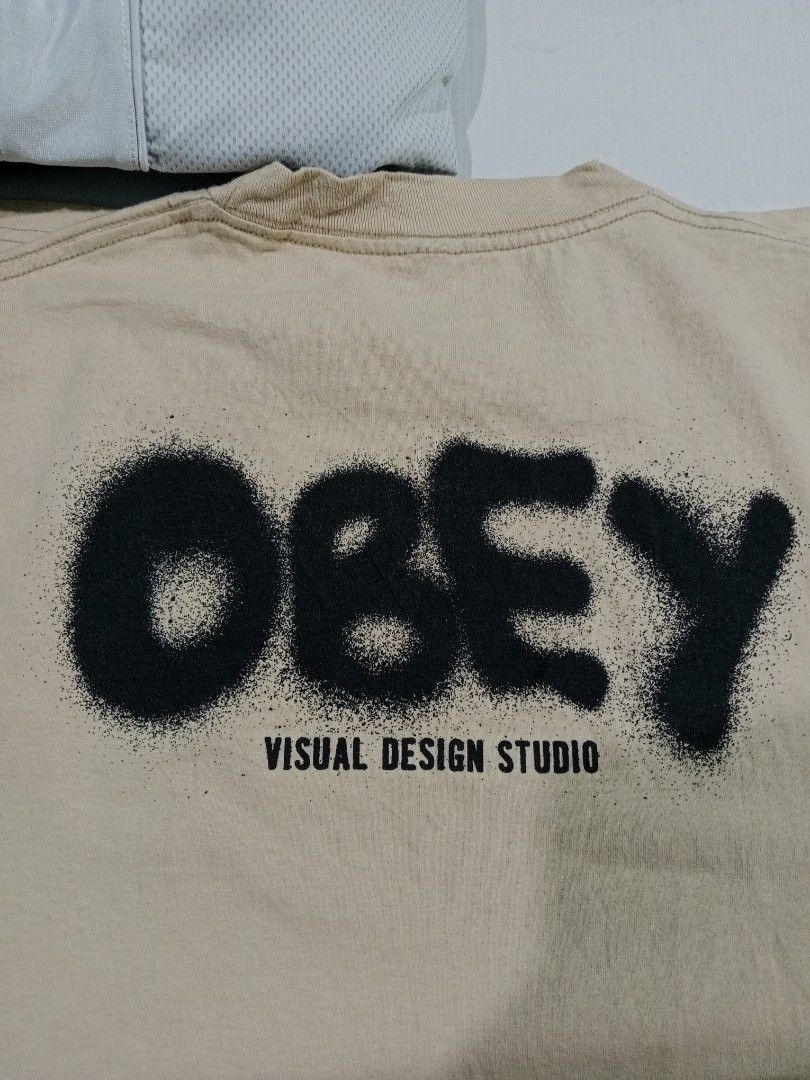 Obey Visual Design Studio Spray Logo T-Shirt Cream (Category: Tshirts & Polo Shirts ) located in Bacolod City. Submitted by jorengrate26639 (Listing ID 1469327113, Image 3). Description: - Brand: Obey - Color: Cream - Size: Medium - Material: 100% cotton, made in Mexico - Design: Black spray-paint logo on chest, large Obey Visual Design Studio graphic on the back - Fit: Standard fit, short sleeves, crew neck - Style: Casual streetwear - Condition