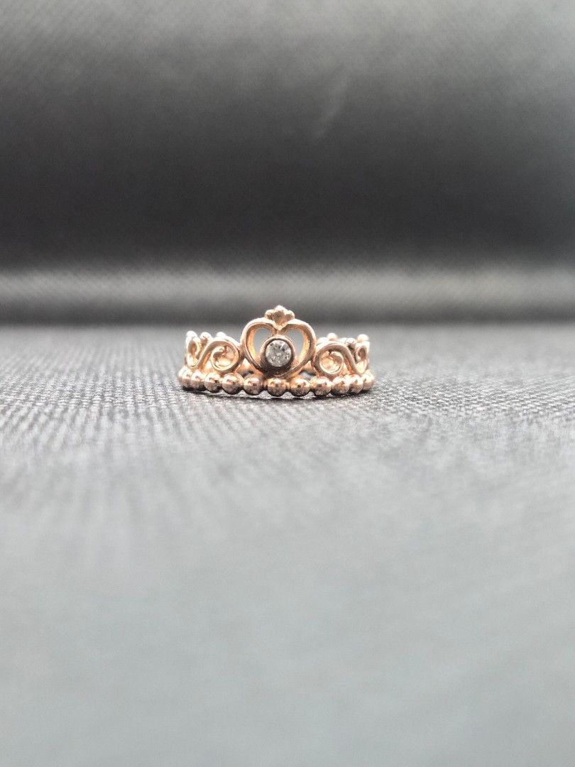 Pandora Rose Gold Princess Crown Ring with Box (Category: Rings) located in Manila. Submitted by prelovedbyc.hannah (Listing ID 1469332191, Image 1). Description: - Brand: Pandora - Material: Rose gold finish - Size: European size 50/ US 5.25-5.5/ 50mm - Design: Princess tiara/crown style with intricate scrollwork and a small clear stone center - Styling: Great for stacking or wearing solo - Inclusions: Original white Pandora box with black velve