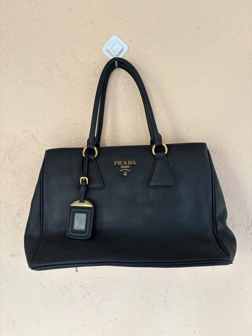 Prada Black Leather Tote Bag (Category: Luxury Bags & Wallets) located in Pozorrubio. Submitted by zionegotthrift (Listing ID 1469198776, Image 1). Description: - Prada tote bag in black grained leather - Elegant gold-toned hardware and dual shoulder straps - Main zipper compartment with smooth Lampo zippers - Includes a stylish luggage tag attached to the front - Interior lined with signature Prada logo fabric - Features an internal leather bran