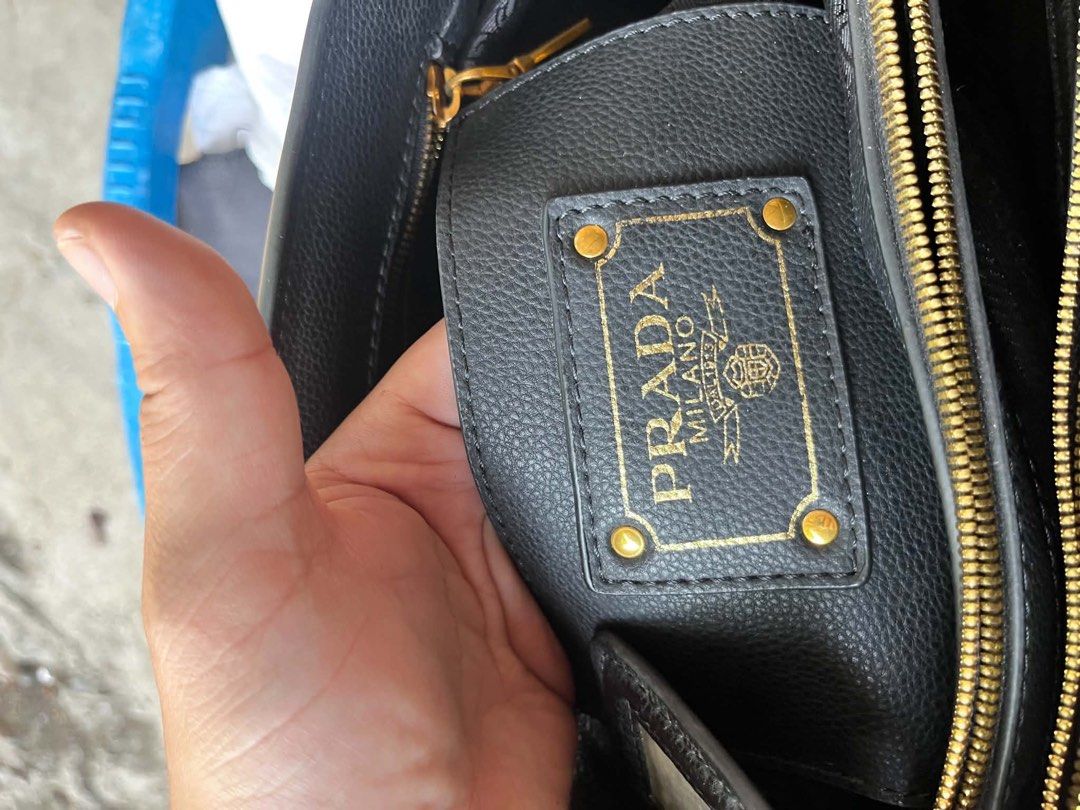 Prada Black Leather Tote Bag (Category: Luxury Bags & Wallets) located in Pozorrubio. Submitted by zionegotthrift (Listing ID 1469198776, Image 3). Description: - Prada tote bag in black grained leather - Elegant gold-toned hardware and dual shoulder straps - Main zipper compartment with smooth Lampo zippers - Includes a stylish luggage tag attached to the front - Interior lined with signature Prada logo fabric - Features an internal leather bran