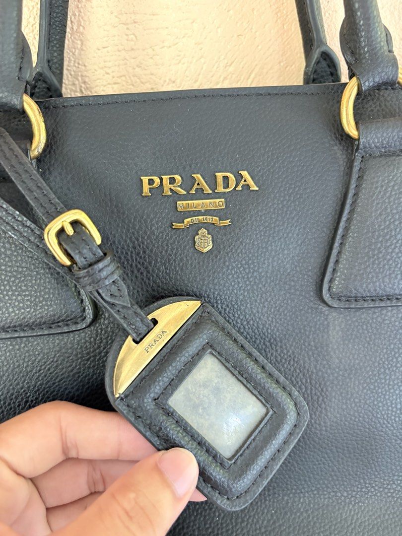 Prada Black Leather Tote Bag (Category: Luxury Bags & Wallets) located in Pozorrubio. Submitted by zionegotthrift (Listing ID 1469198776, Image 2). Description: - Prada tote bag in black grained leather - Elegant gold-toned hardware and dual shoulder straps - Main zipper compartment with smooth Lampo zippers - Includes a stylish luggage tag attached to the front - Interior lined with signature Prada logo fabric - Features an internal leather bran