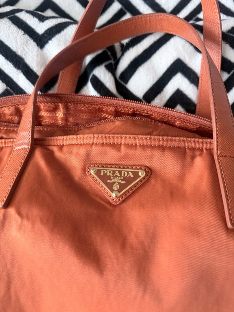 Prada nylon tote bag orange with strap (Category: Luxury Bags & Wallets) located in Pasig City. Submitted by sherill888 (Listing ID 1469338273, Image 3). Description: - Authentic Prada orange nylon tote bag - Saffiano leather trim & gold-tone hardware - Iconic front triangle logo plaque - Matching top handles & detachable crossbody strap for versatile wear - Secure top zip closure - Signature Prada fabric-lined interior with a roomy everyday size