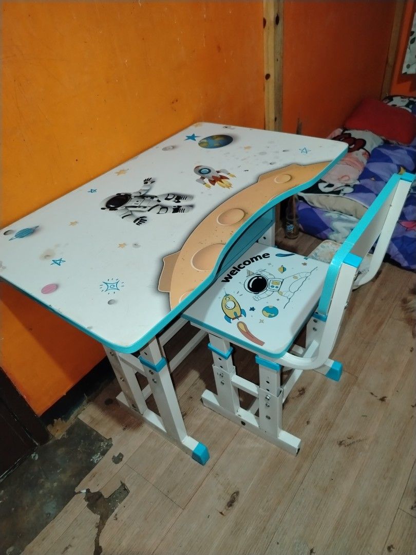 Space theme kids study table and matching chair set (Category: Kids Tables & Chairs) located in Manila. Submitted by nesacake (Listing ID 1469335387, Image 1). Description: - Kids study table and matching chair set with fun space exploration theme (astronauts, rockets, planets) - White surfaces with blue edges and matching space print seat - Includes attached hutch with built-in bookshelf compartments and holders - Sturdy metal frame with adjusta