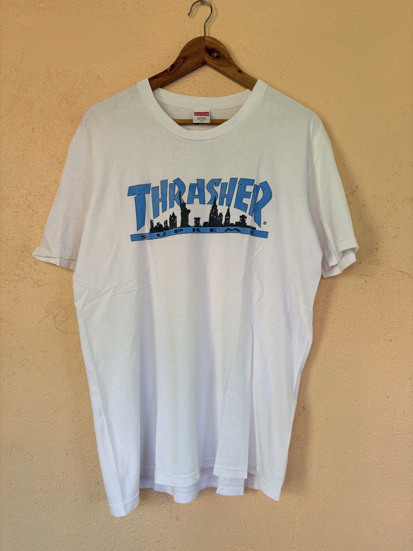 Supreme x Thrasher Skyline White T-Shirt Medium (Category: Tshirts & Polo Shirts ) located in Pozorrubio. Submitted by zionegotthrift (Listing ID 1469200485, Image 1). Description: - Brand: Supreme x Thrasher - Color: White - Size: Medium (M) - Design: Blue Thrasher text graphic over black NY skyline silhouette with Supreme red box logo neck tag - Material: 100% pre-shrunk cotton - Origin: Made in USA - Condition: 100% authentic and well-maintain