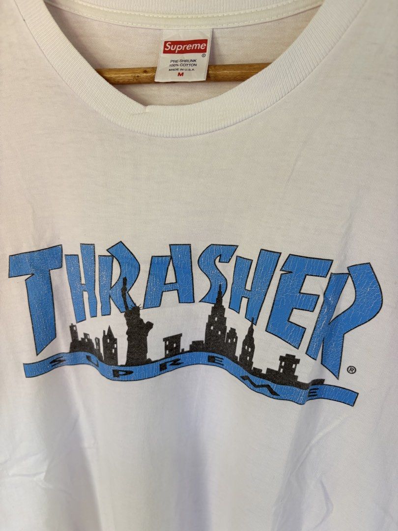 Supreme x Thrasher Skyline White T-Shirt Medium (Category: Tshirts & Polo Shirts ) located in Pozorrubio. Submitted by zionegotthrift (Listing ID 1469200485, Image 2). Description: - Brand: Supreme x Thrasher - Color: White - Size: Medium (M) - Design: Blue Thrasher text graphic over black NY skyline silhouette with Supreme red box logo neck tag - Material: 100% pre-shrunk cotton - Origin: Made in USA - Condition: 100% authentic and well-maintain