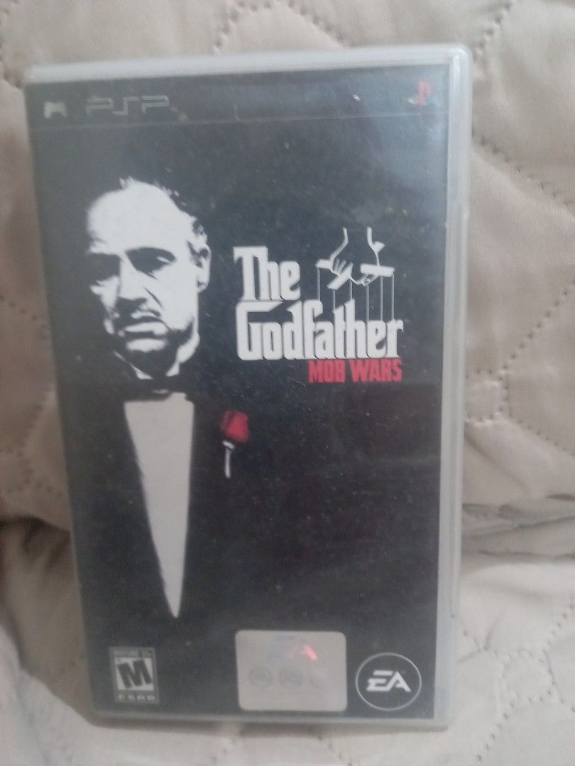 The Godfather PSP Game (Category: PlayStation) located in Valenzuela. Submitted by retro.rush (Listing ID 1469313446, Image 1). Description: - Game: The Godfather - Platform: Psp - Packaging: Standard keep case with minor dust and wear on the plastic sleeve - Features: Includes gameplay screenshots and "Welcome to the Family" text on the back cover - Publishers/Licensors: EA and Paramount logos present - Condition: Good, playable condition (ideal