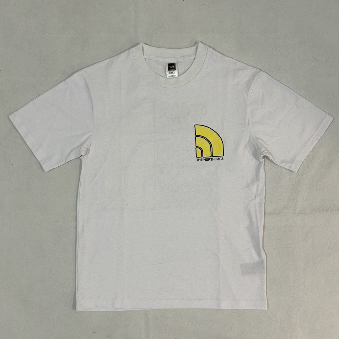 The North Face White Graphic T-Shirt Medium (Category: Tshirts & Polo Shirts ) located in Cavite. Submitted by moo2k (Listing ID 1469204358, Image 1). Description: - Brand: The North Face - Size: Medium (tag on collar) - Color: White - Design: Yellow dome logo on front, large grey brand text and yellow dome graphic on back - Fit: Short sleeves, standard crew neck - Condition: Clean fabric, no stains or wear detected.