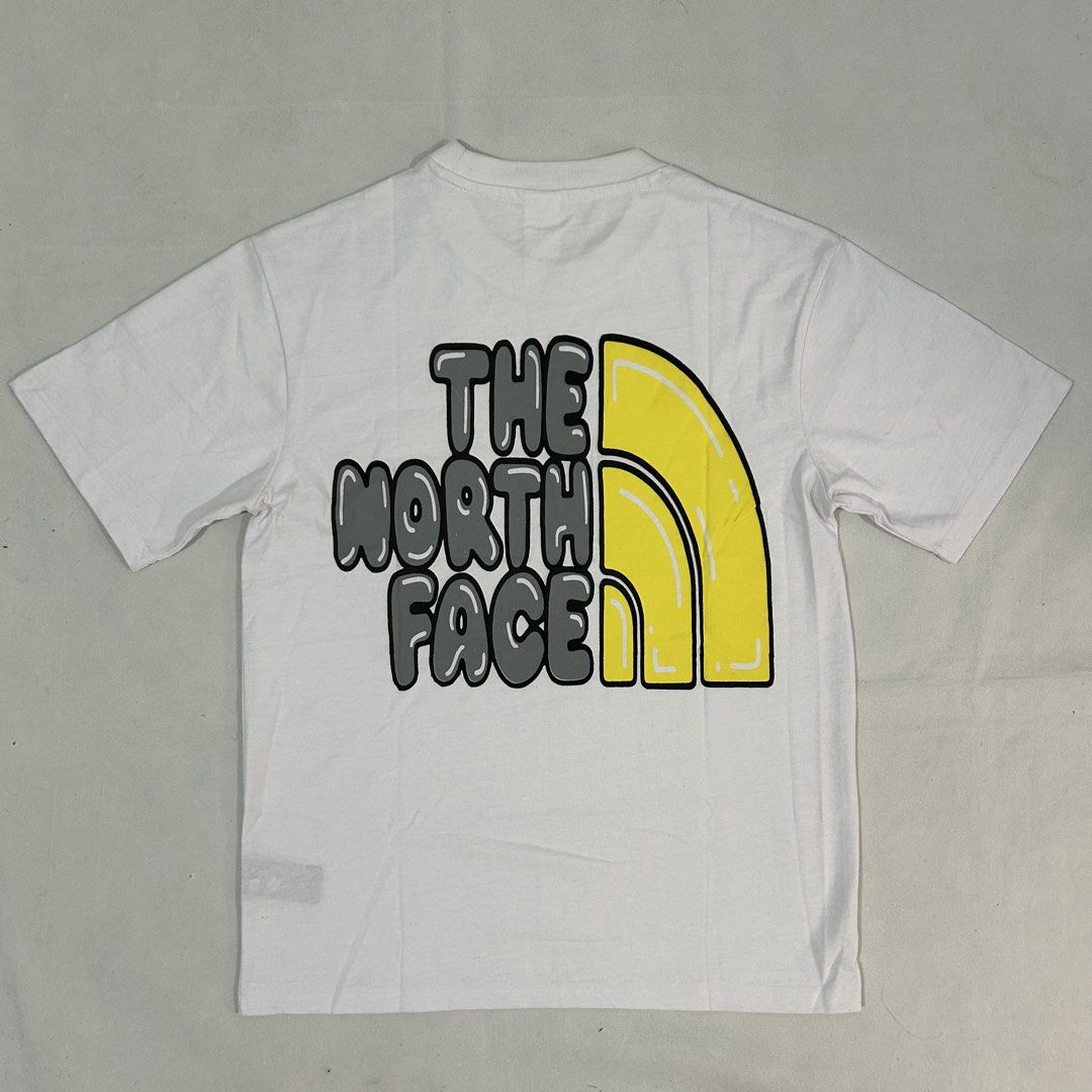 The North Face White Graphic T-Shirt Medium (Category: Tshirts & Polo Shirts ) located in Cavite. Submitted by moo2k (Listing ID 1469204358, Image 2). Description: - Brand: The North Face - Size: Medium (tag on collar) - Color: White - Design: Yellow dome logo on front, large grey brand text and yellow dome graphic on back - Fit: Short sleeves, standard crew neck - Condition: Clean fabric, no stains or wear detected.