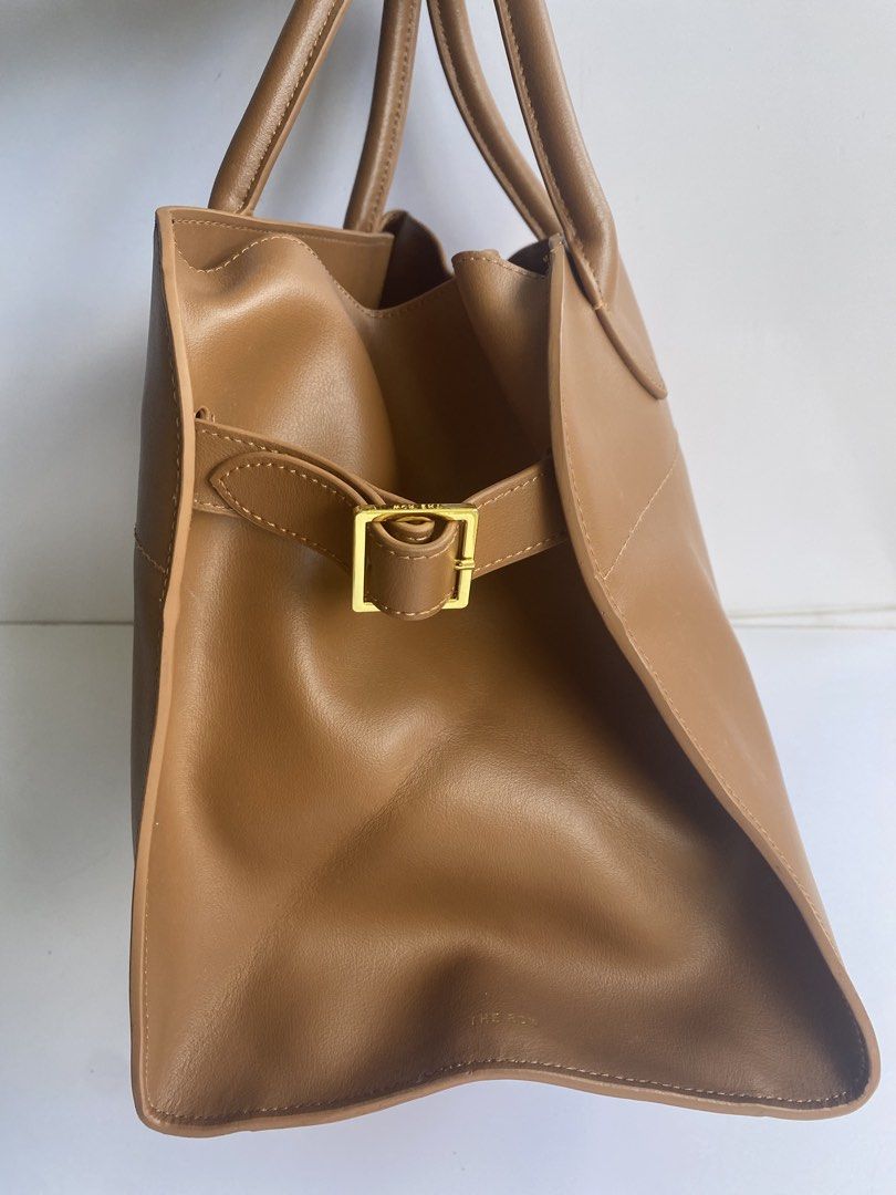 The Row Margaux 15 Leather Bag (Category: Tote Bags) located in Cavite. Submitted by benta_bounce (Listing ID 1469228971, Image 3). Description: - Brand: The Row - Measurements: 38 x 28 x 22.85 cm - Material: Rich brown leather - Style: Structured tote bag with minimalist design - Features: Dual top handles, gold-tone buckle side straps, and protective metal feet on the base - Condition: Clean interior and crisp exterior finishing - Perfect for: 