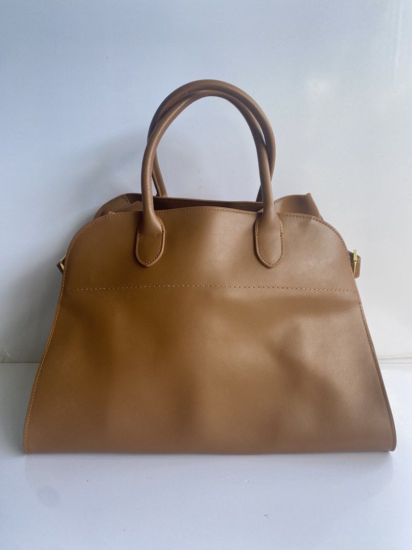 The Row Margaux 15 Leather Bag (Category: Tote Bags) located in Cavite. Submitted by benta_bounce (Listing ID 1469228971, Image 2). Description: - Brand: The Row - Measurements: 38 x 28 x 22.85 cm - Material: Rich brown leather - Style: Structured tote bag with minimalist design - Features: Dual top handles, gold-tone buckle side straps, and protective metal feet on the base - Condition: Clean interior and crisp exterior finishing - Perfect for: 
