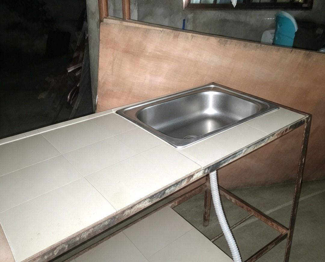 Tiled Kitchen Sink Station with Metal Frame (Category: Bathroom & Kitchen Fixtures) located in Manila. Submitted by jadestcne (Listing ID 1469195113, Image 2). Description: - Durable metal frame prep station with minor surface wear - Integrated stainless steel sink for washing and prep - Easy-to-clean white tiled top surface and lower storage shelf - Includes flexible corrugated drainage hose underneath - Perfect for outdoor cooking, utility room