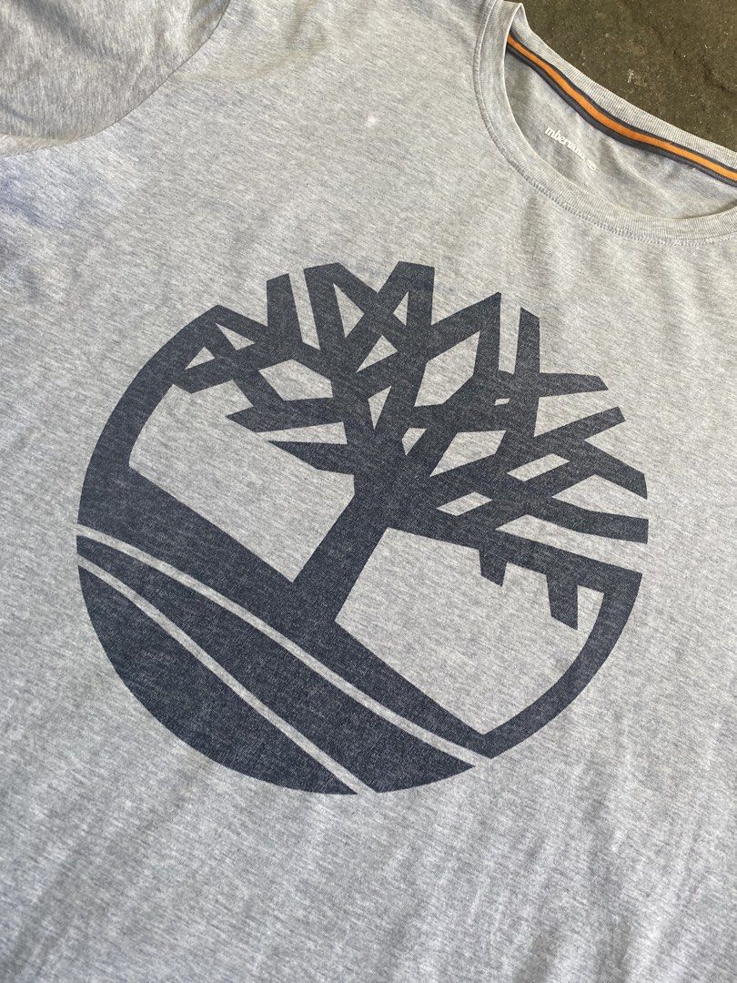 Timberland Grey Logo T-Shirt (Category: Tshirts & Polo Shirts ) located in Caloocan City. Submitted by remythrift (Listing ID 1469203111, Image 3). Description: - Brand: Timberland - Color: Grey with large tree logo graphic - Size: Medium (tag printed inside neckline) - Details: Crew neck with orange and dark grey stripe inner collar taping - Material: Soft cotton fabric - Condition: Good overall, but note two small holes near the bottom hem line