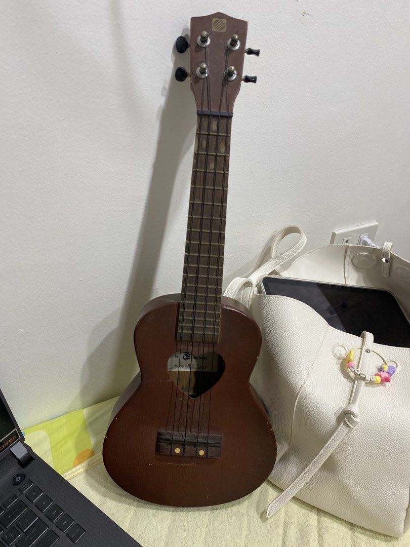 UKE BOX Ukulele Model UKE Love (Category: Musical Instruments) located in Manila. Submitted by vintageonlinee (Listing ID 1469233948, Image 3). Description: - Brand: UKE BOX (Model: UKE Love) - Color/Style: Brown acoustic ukulele with a unique heart-shaped soundhole - Build: Standard size, wooden fretboard with frets, and reliable tuning pegs - Strings: 4 standard nylon strings installed - Condition: Minor scuffs and marks from normal handling an