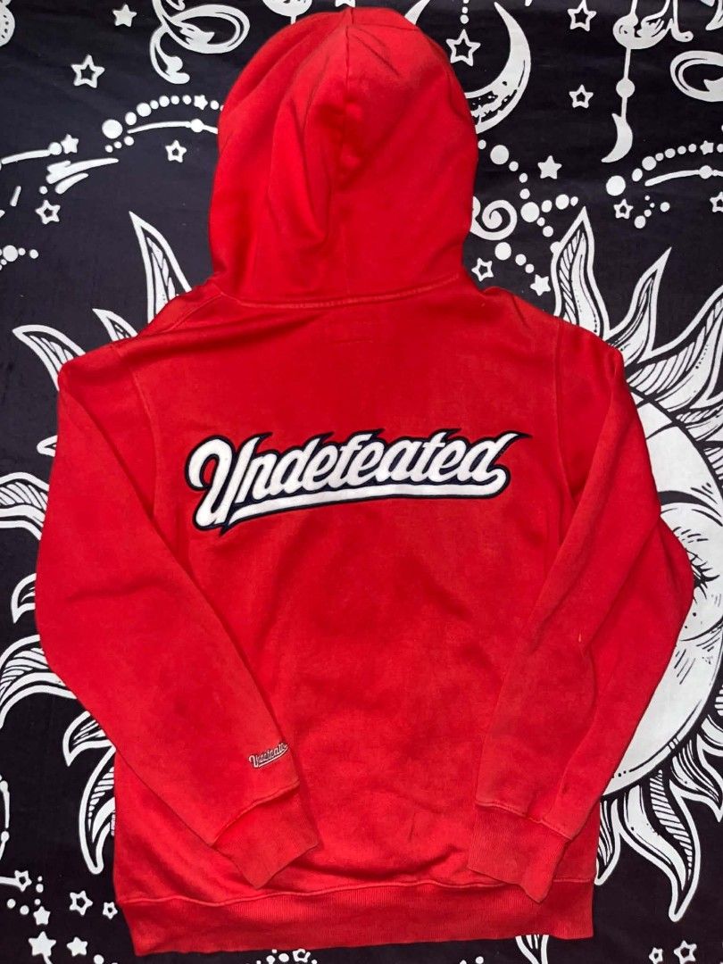 Undefeated Red Hoodie Size M (Category: Hoodies) located in Manila. Submitted by joshua_varona11 (Listing ID 1469208016, Image 2). Description: - Brand: Undefeated - Color: Bright red with white and pink details - Size: Medium - Design: Large embroidered white logo on the back, smaller chest logo - Features: Pink drawstrings, front kangaroo pocket, ribbed cuffs - Interior: Soft fleece lining - Style: Essential streetwear layering piece.
