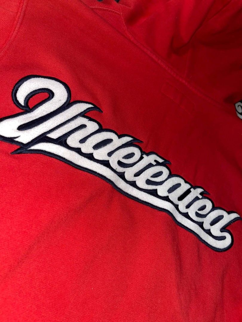 Undefeated Red Hoodie Size M (Category: Hoodies) located in Manila. Submitted by joshua_varona11 (Listing ID 1469208016, Image 3). Description: - Brand: Undefeated - Color: Bright red with white and pink details - Size: Medium - Design: Large embroidered white logo on the back, smaller chest logo - Features: Pink drawstrings, front kangaroo pocket, ribbed cuffs - Interior: Soft fleece lining - Style: Essential streetwear layering piece.