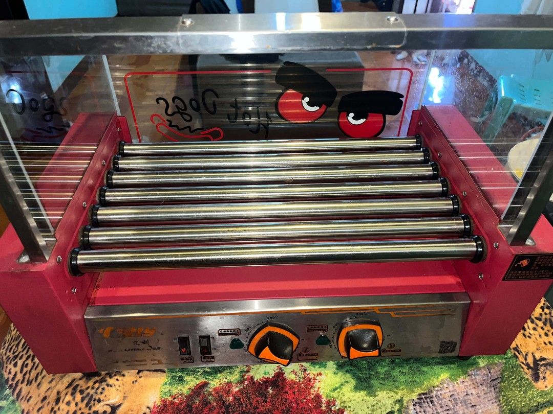 Verly 7 Pin Hotdog Roller Grill Machine (Category: BBQ, Grills & Hotpots) located in Manila. Submitted by iamgraceco16493 (Listing ID 1469164156, Image 2). Description: - 7 heavy-duty stainless steel rollers for even cooking - Eye-catching red base with clear glass display cover - Front temperature control knobs for easy heat management - Dual power switches with handy indicator lights - Fun 'Hot Dogs' graphic decal on the glass - Ideal for conve