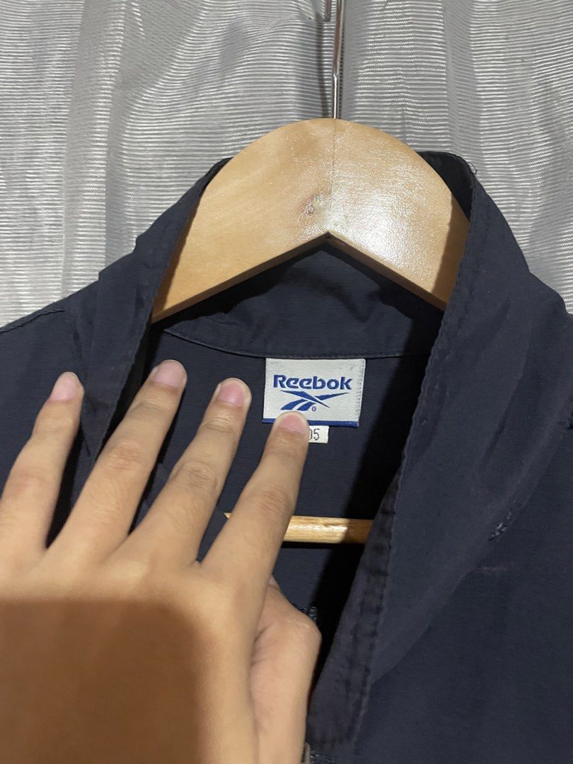 Vintage Reebok Navy Windbreaker Jacket (Category: Coats, Jackets and Outerwear) located in Calbayog City. Submitted by thriftme.bro (Listing ID 1469324471, Image 3). Description: Navy blue Reebok windbreaker in size 105. Features a full zip, high neck, and embroidered logos on the chest and sleeve. Lightweight and easy to layer..