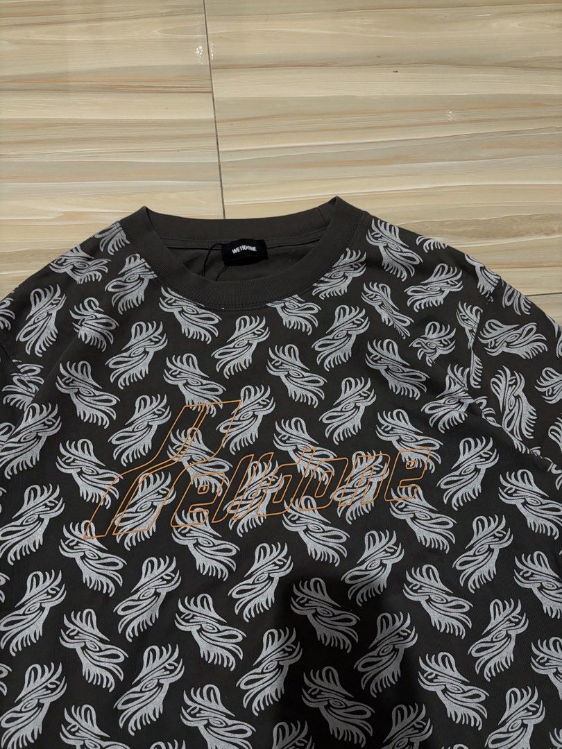 We11done All-Over Print T-Shirt Size M (Category: Tshirts & Polo Shirts ) located in Ajuy. Submitted by reeyn0515 (Listing ID 1469326090, Image 2). Description: - 20.5x26.5 - Brand: We11done - Color: Dark grey with striking tribal-style graphic print - Size: Medium (M) - Details: Contrast orange embroidered logo on chest, classic crew neck - Authenticity: Includes original neck tags, interior care tags with batch code WD-TP6-20-074-U-3K, and auth