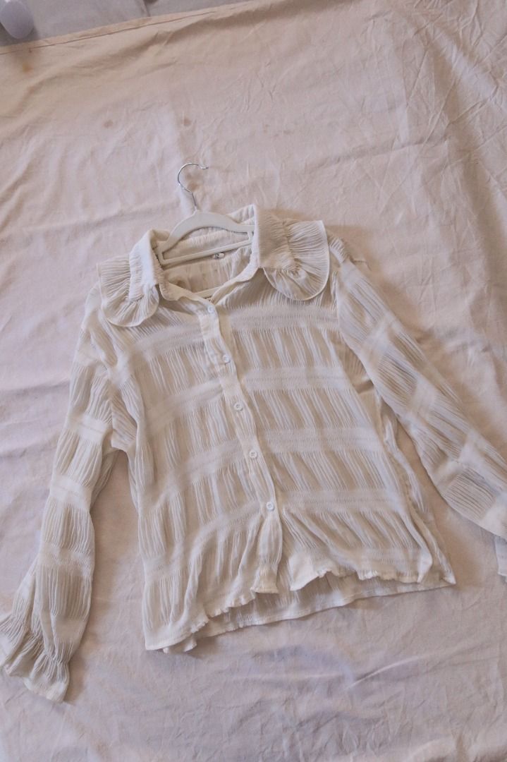White Ruffle Collar Button-Down Blouse Long Sleeve (Category: Blouses) located in Manila. Submitted by imama23 (Listing ID 1469197311, Image 1). Description: - Color: White - Style: Vintage-inspired button-down blouse with textured pleated panels - Details: Large statement ruffle collar, flared cuffs, and front button closure - Fabric: Lightweight and slightly sheer Condition: 8/10 Size: M-L Location: Manila (near taft) 📦 SHIPPING • Full payment