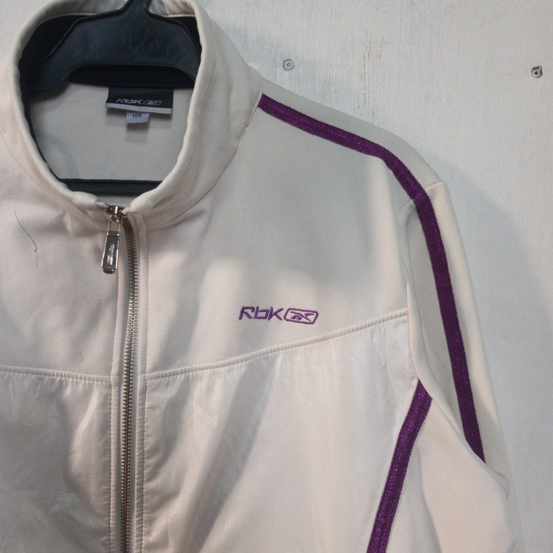 Y2K-era Reebok track jacket (Category: Coats, Jackets and Outerwear) located in Manila. Submitted by joefrey12 (Listing ID 1469238622, Image 2). Description: - Authentic white Reebok track jacket - Dimes 21x24.5 - Eye-catching purple glitter piping on sleeves and chest - Contrast dark navy cuffs and collar trim - Purple RBK embroidered logo on right chest with fancy silver-stitched RBK embroidery near the left shoulder - Full front zip closure wi
