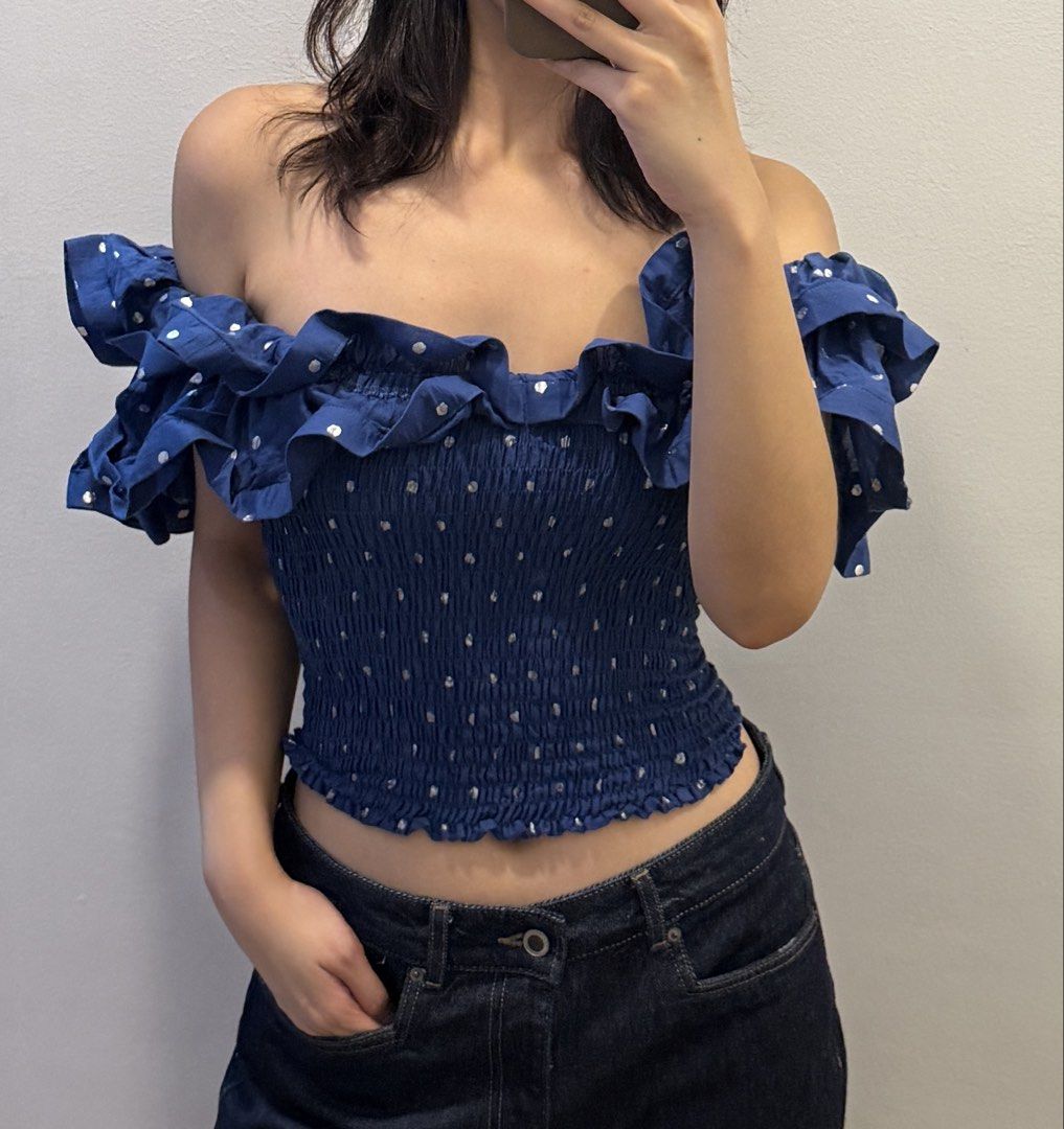 Yong studio isadora top (Category: Sleeveless) located in Manila. Submitted by shopelisse (Listing ID 1469296770, Image 1). Description: - Color/Pattern: Blue with white polka dots - Style: Off-shoulder crop top with ruffle sleeves and neckline - Fit: Stretchy, smocked elastic body for a snug fit - Condition: Worn once for a quick photo, flawless - Styling Tip: Pairs perfectly with high-waisted denim jeans.