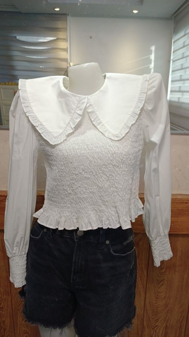 ZARA White Blouse with Oversized Ruffle Collar (Category: Blouses) located in General Santos City (Dadiangas). Submitted by amzonshop (Listing ID 1469239348, Image 2). Description: - Color: White - Design: Wide ruffle collar and smocked body - Sleeves: Long sleeves with ruffled cuffs - Closure: Back zipper - Styling: Great to pair with denim shorts or skirts for a casual look .
