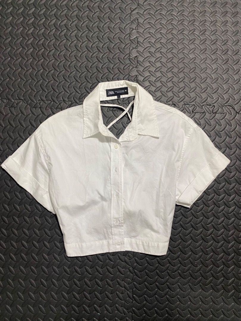 Zara White Cropped Button-Up Shirt (Category: Shirts) located in Manila. Submitted by everydrei (Listing ID 1469203968, Image 1). Description: - Brand: Zara - Color: White - Material: Structured cotton - Style: Crop top with short sleeves (folded cuffs), standard collar, and button-down front - Special Detail: Unique criss-cross strap design at the back neckline - Fit: True to size, looks great with high-waisted bottoms.