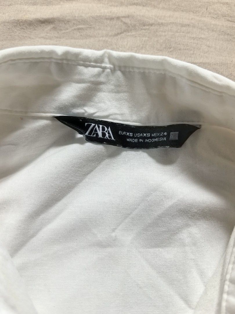 ZARA White Wrap Shirt Size XS (Category: Blouses) located in Tacloban City. Submitted by thead.declutters (Listing ID 1469217989, Image 3). Description: - Brand: ZARA - Color: Classic White - Size: EUR XS / US XS / MEX 24 - Design: Asymmetric wrap front with stylish tie closures - Details: Long sleeves with cuffed wrists and high-low curved hemline - Origin: Made in Indonesia - Condition: Clean, minimal look - Styling: Highly versatile; easily pa