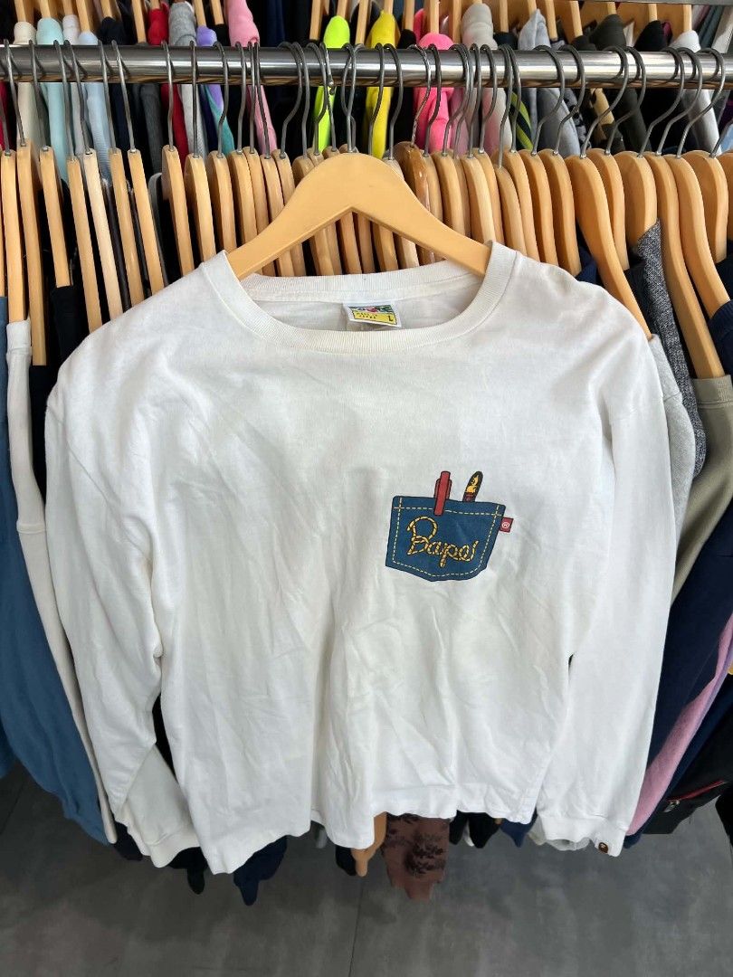 A Bathing Ape Bape Pocket Graphic Long Sleeve Tee (Category: Tshirts & Polo Shirts ) located in Urdaneta. Submitted by jayceegarage (Listing ID 1469543807, Image 1). Description: - Brand: A Bathing Ape (Bape) - Item: White Long Sleeve Shirt - Size: L - Material: 100% Cotton (Made in Japan) - Design: Front graphic of denim pocket with red pen and lighter, plus yellow rope Bape branding - Details: Iconic Bape collar tag, gold ape head washing label