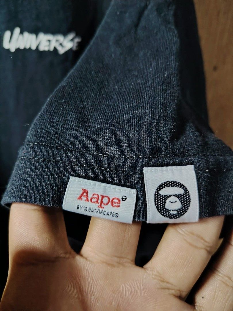 Aape By A Bathing Ape Black T-shirt (Category: Tshirts & Polo Shirts ) located in Manila. Submitted by tabuzomaria1422 (Listing ID 1469451832, Image 3). Description: - Brand: Aape by A Bathing Ape - Color: Black - Material: 100% Cotton - Design: "Somewhere in the Aape Universe" text on chest - Back: Large graphic print with Aape branding and signature ape head logo - Details: Woven Aape logo tabs on the sleeve - Condition: Brand new / Excellent q