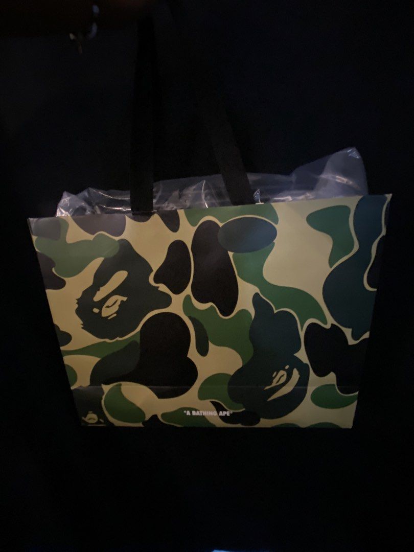 AAPE By A Bathing Ape Camo Tote Bag (Category: Tote Bags) located in Quezon City. Submitted by gabdiorr666 (Listing ID 1469505276, Image 2). Description: - Brand: AAPE by A Bathing Ape - Design: Classic olive drab woodland camouflage print - Material: Durable, sturdy nylon fabric - Features: Multiple exterior utility pockets, webbed carry handles, front branded white text patch, and iconic ape head logo tag - Inclusions: Comes with original AAPE 