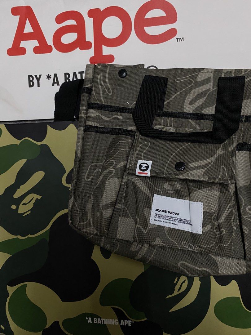 AAPE By A Bathing Ape Camo Tote Bag (Category: Tote Bags) located in Quezon City. Submitted by gabdiorr666 (Listing ID 1469505276, Image 3). Description: - Brand: AAPE by A Bathing Ape - Design: Classic olive drab woodland camouflage print - Material: Durable, sturdy nylon fabric - Features: Multiple exterior utility pockets, webbed carry handles, front branded white text patch, and iconic ape head logo tag - Inclusions: Comes with original AAPE 