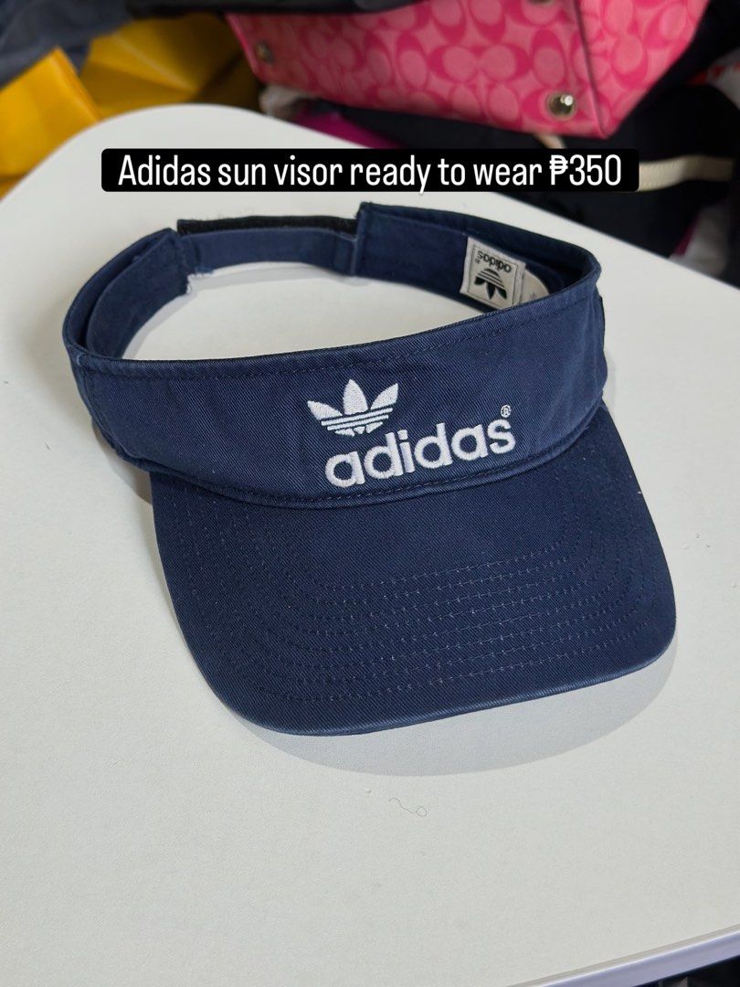 Adidas Navy Blue Sun Visor (Category: Caps & Hats) located in Daet. Submitted by thrifthings2018 (Listing ID 1469466848, Image 1). Description: - Brand: Adidas - Color: Navy blue with white embroidered trefoil logo - Material: 100% cotton - Size: Adjustable velcro strap for a customized fit - Condition: Clean interior tags visible - Ideal for: Sunny days, running, and outdoor activities.