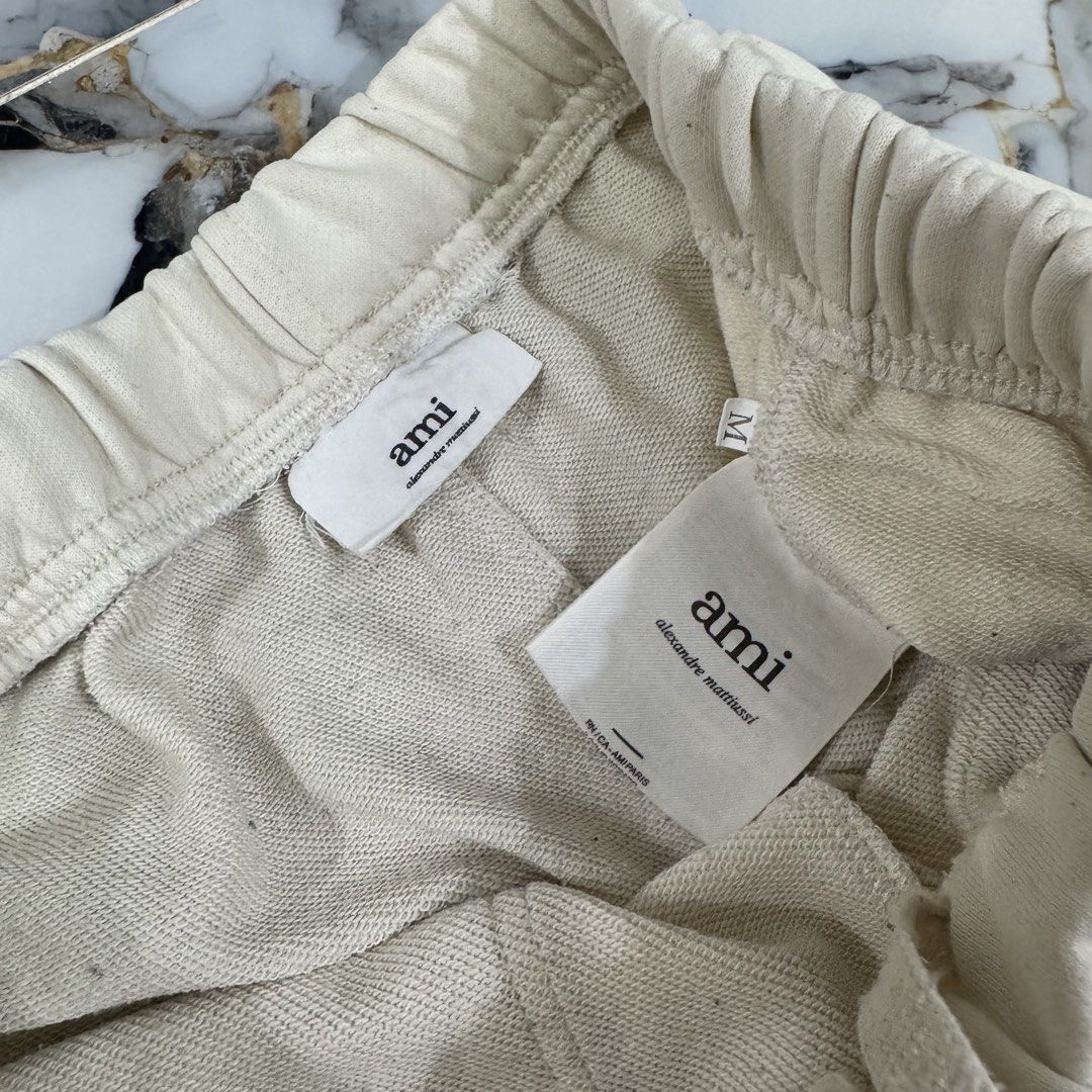 Ami Paris Cream Sweatshorts Size M (Category: Shorts) located in Manila. Submitted by fastflip.ph (Listing ID 1469429506, Image 3). Description: - Brand: Ami Alexandre Mattiussi - Size: M - Color: Cream - Material: Soft cotton fleece - Waist: Elastic with drawstring - Details: Large front patch pockets, rhinestone heart logo near left hem, side slits at bottom.