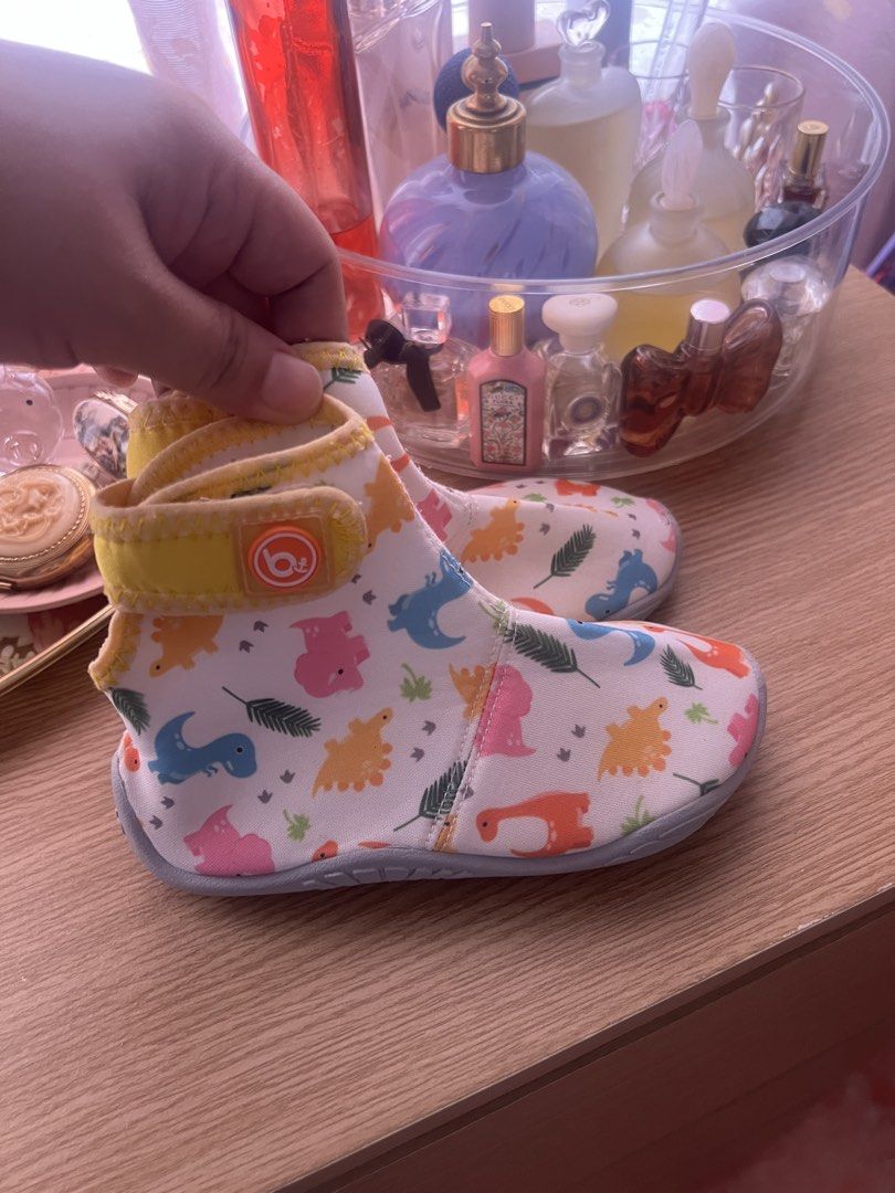 AQUA Booties Soft Sole Shoes (Category: Babies & Kids Fashion) located in Cebu City. Submitted by shofaholicz (Listing ID 1469457137, Image 2). Description: - Brand: Bay.b - Design: Colorful dinosaur and leaf print on a white base with yellow trim - Sole: Soft sole with embossed bay.b logo and non-slip grip dots - Closure: Easy slip-on style with a secure velcro strap - Condition: Brand new and comfortable for babies.