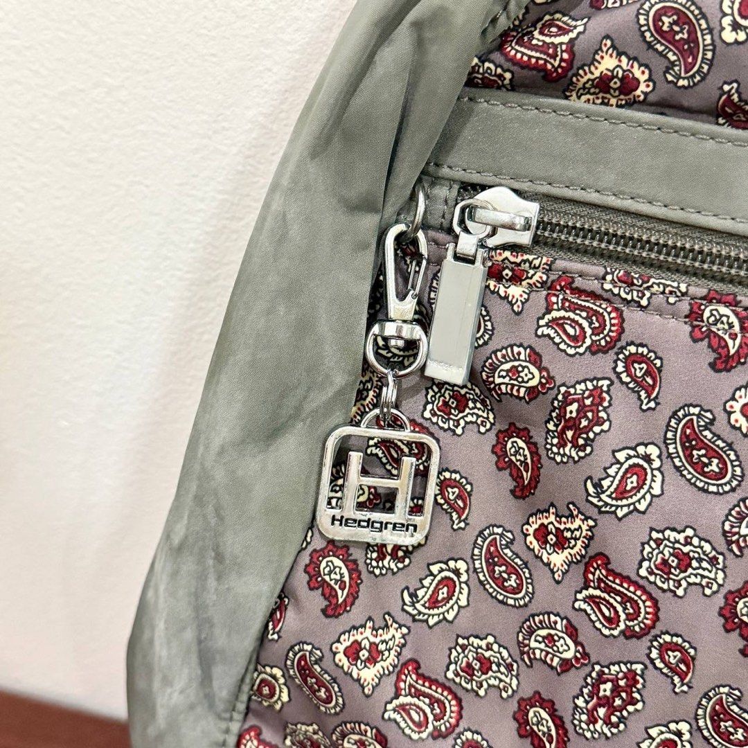 [Authentic] Used Hedgren Gray Paisley Print Nylon Backpack Floral Pattern Lightweight Bag (Category: Backpacks) located in Quezon City. Submitted by brandedusagoodies (Listing ID 1469552322, Image 2). Description: Used Hedgren backpack featuring a gray base with a red, cream, and burgundy paisley print, complemented by muted green panels. It has a front zippered pocket, metallic Hedgren logo and keychain charm, side pockets, adjustable shoulder s