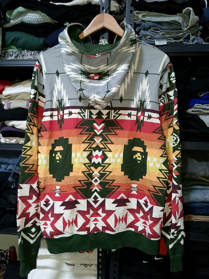 BAPE Aztec Geometric Pattern Full Zip Hoodie (Category: Hoodies) located in Manila. Submitted by mjthrifted_second (Listing ID 1469409384, Image 2). Description: - Brand: BAPE (A Bathing Ape) - Design: Bold aztec geometric pattern across front, back, and sleeves -Dimes: 22/27.5 - Colorway: Grey hood, red/yellow midsection, and dark green ribbing - Details: Signature Ape head graphic integrated into the sides - Closure: Full zip up to the chin - C