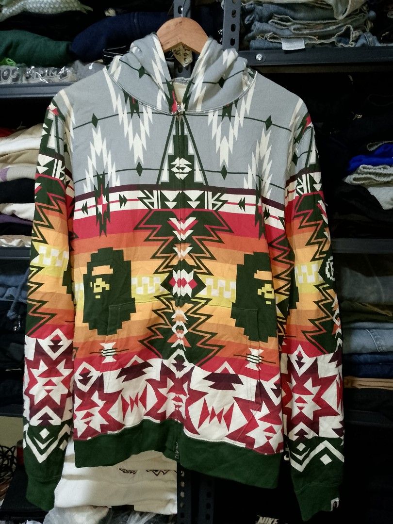 BAPE Aztec Geometric Pattern Full Zip Hoodie (Category: Hoodies) located in Manila. Submitted by mjthrifted_second (Listing ID 1469409384, Image 1). Description: - Brand: BAPE (A Bathing Ape) - Design: Bold aztec geometric pattern across front, back, and sleeves -Dimes: 22/27.5 - Colorway: Grey hood, red/yellow midsection, and dark green ribbing - Details: Signature Ape head graphic integrated into the sides - Closure: Full zip up to the chin - C