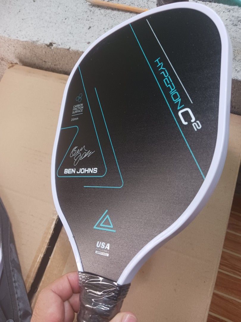 Ben Johns Hyperion C2 Pickleball Paddle (Category: Racket and Ball Sports) located in Cebu City. Submitted by joecristinesayson (Listing ID 1469570542, Image 2). Description: - Model: Ben Johns Hyperion C2 - Surface & Core: Carbon friction surface, 16mm thickness - Certification: USA Pickleball approved stamp - Condition: Brand new, handle still wrapped in original plastic - Inclusions: Includes two pickleballs and a carrying case - Status: Game-