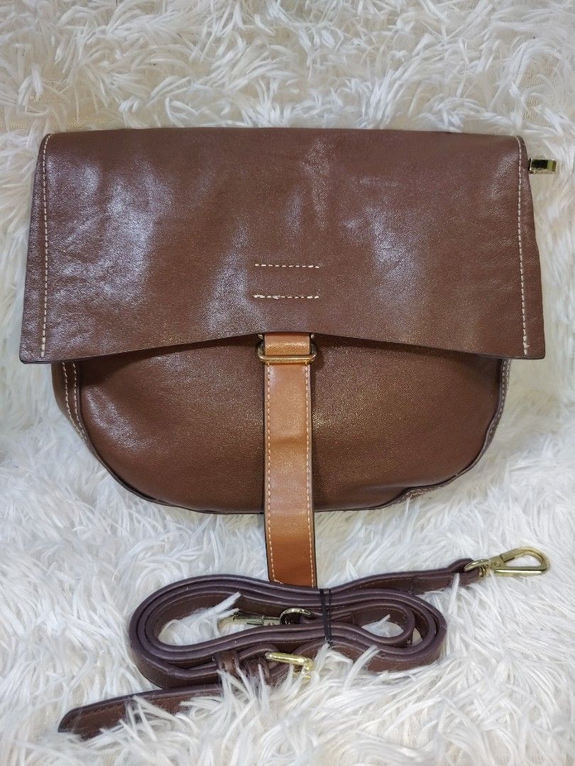 Brown Leather Crossbody Bag with Flap Closure (Category: Cross-body Bags) located in Quezon City. Submitted by zhelcloset01 (Listing ID 1469506044, Image 1). Description: - Material: Genuine brown leather with stylish white contrast stitching - Design: Unique curved bottom shape with a secure front flap and vertical lighter brown strap - Hardware: Premium gold-tone metal clasps - Strap: Adjustable matching shoulder strap for comfortable wear - In