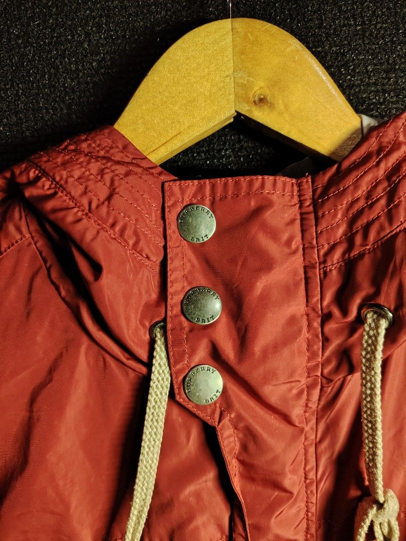 Burberry Brit Red Hooded Windbreaker Jacket (Category: Coats, Jackets and Outerwear) located in Baguio. Submitted by angeloshoppebaguio2600 (Listing ID 1469480133, Image 3). Description: - Brand: Burberry Brit - Color: Rich red with classic check pattern lining - Material: Lightweight and durable nylon - Features: Branded metal snap buttons, adjustable drawstrings at hood and hem, and exterior pockets - Details: Signature leather logo patch near 