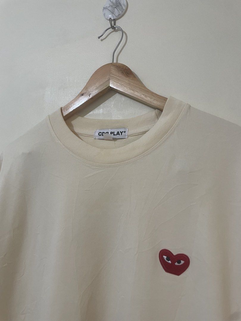 CDG PLAY Heart Logo Tee Cream Size L (Category: Activewear) located in Davao. Submitted by thegraildept2026 (Listing ID 1469415744, Image 2). Description: - Brand: Comme des Garçons PLAY - Color: Soft cream - Size: L (170/88A) - Design: Embroidered red heart logo patch on chest - Material: Comfortable cotton jersey - Condition: Clean collar tag, great basic piece for everyday wear.